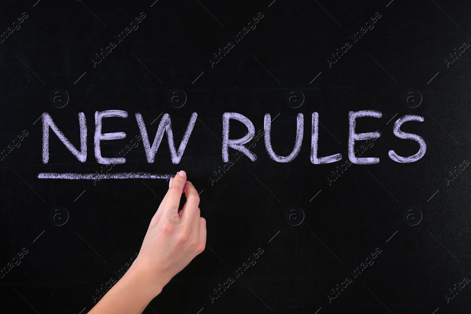 Image of Woman writing text NEW RULES on chalkboard, closeup