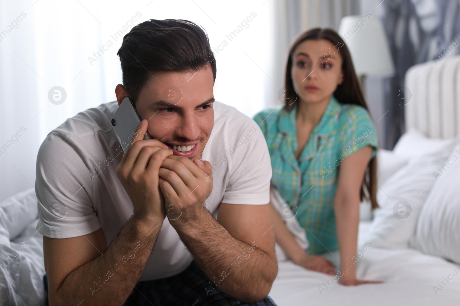 Photo of Distrustful young woman eavesdropping on boyfriend at home. Jealousy in relationship
