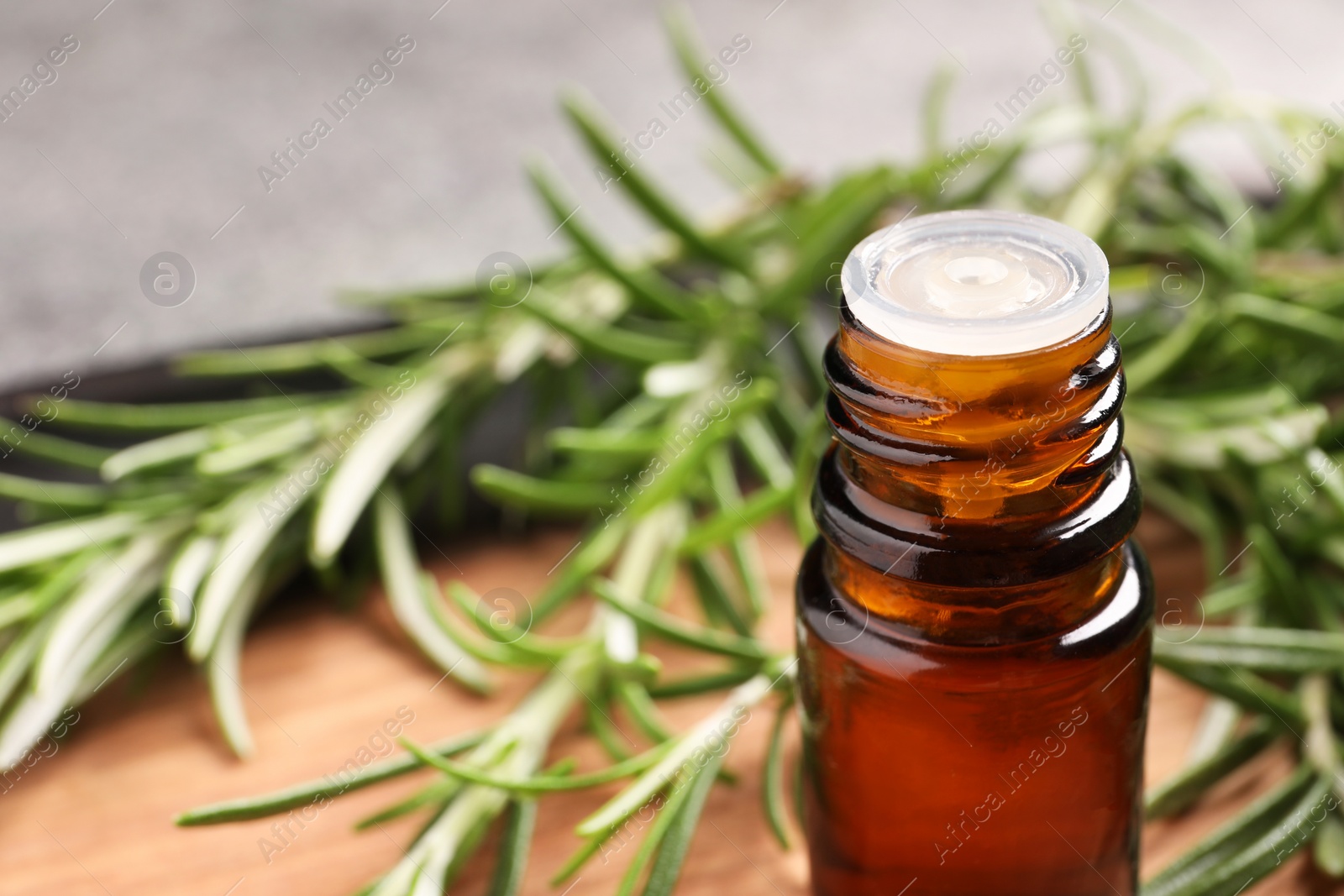 Photo of Bottle of essential oil and fresh rosemary on board, closeup. Space for text