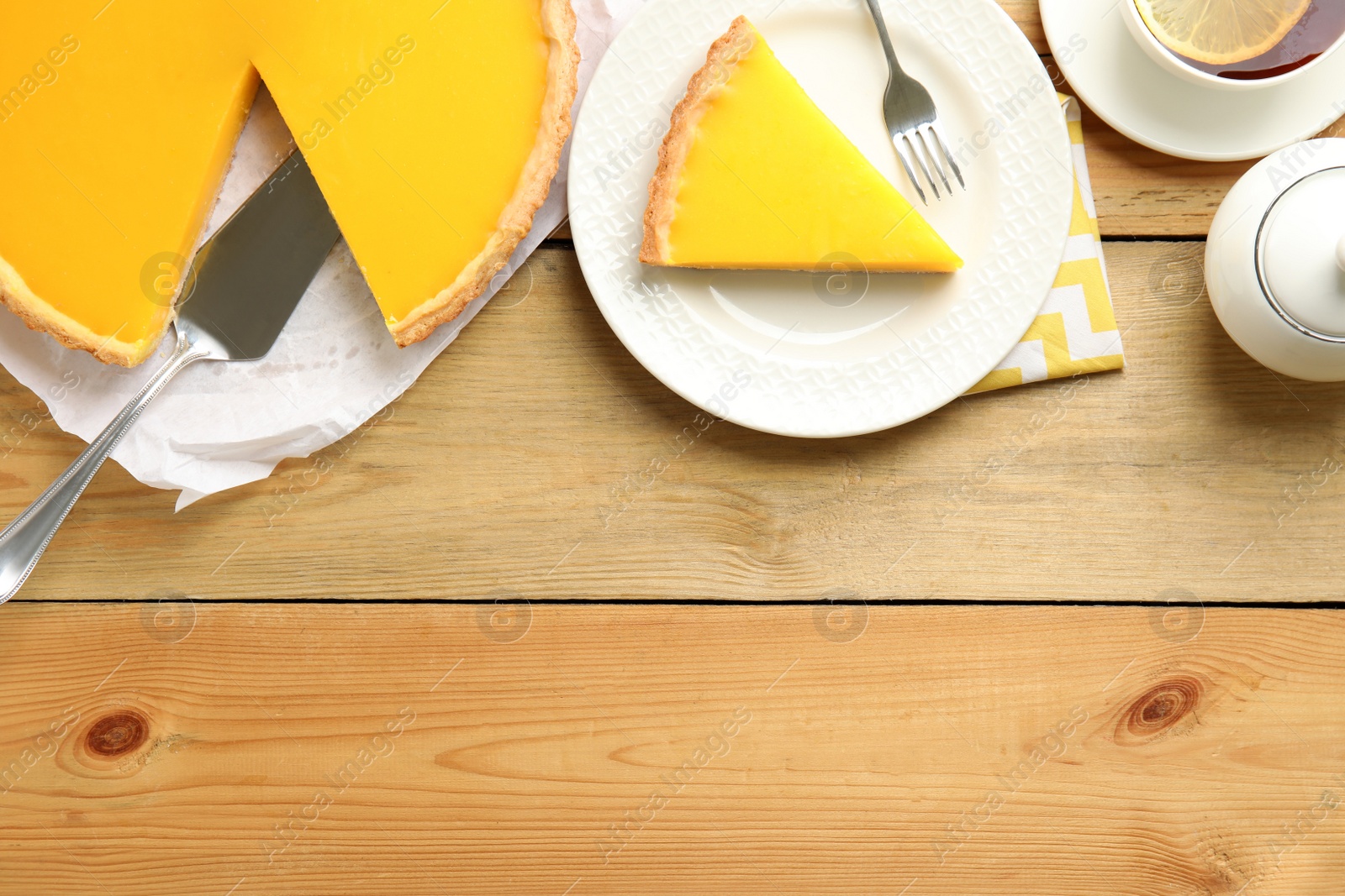 Photo of Delicious homemade lemon pie and tea on wooden table, flat lay. Space for text