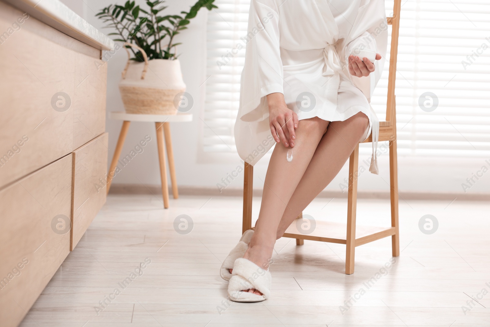 Photo of Young woman applying body cream onto leg in bathroom, closeup. Space for text