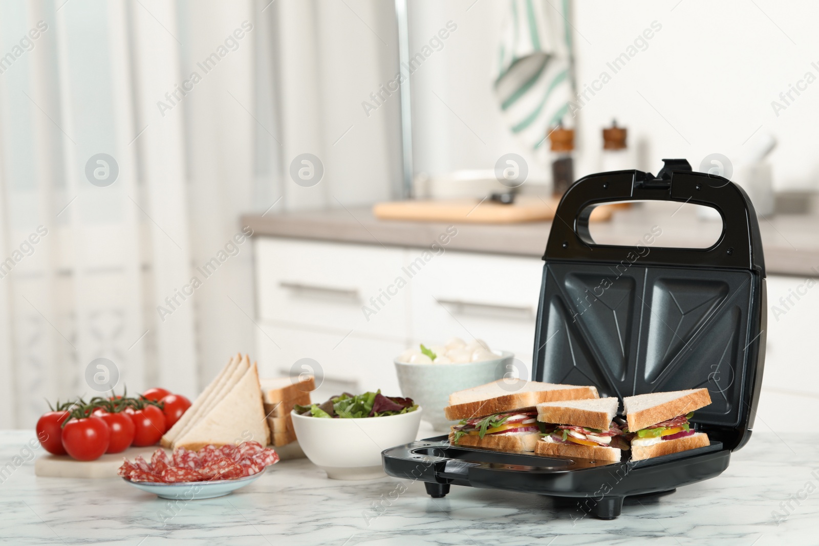 Photo of Modern grill maker with sandwiches and different products on white marble table in kitchen