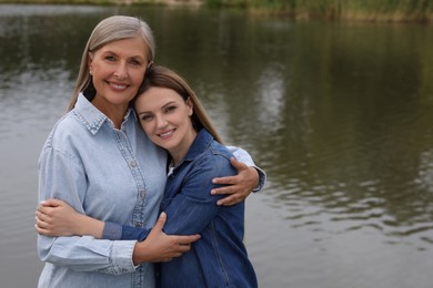 Happy mature mother and her daughter hugging near pond, space for text