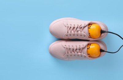 Pair of stylish shoes with modern electric footwear dryer on light blue background, top view. Space for text