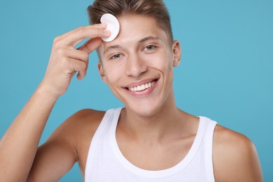 Photo of Handsome man cleaning face with cotton pad on light blue background