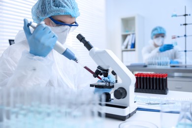 Scientist dripping sample onto glass slide while working with microscope in laboratory