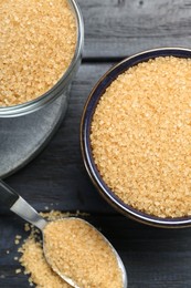 Brown sugar in bowls and spoon on black wooden table, flat lay