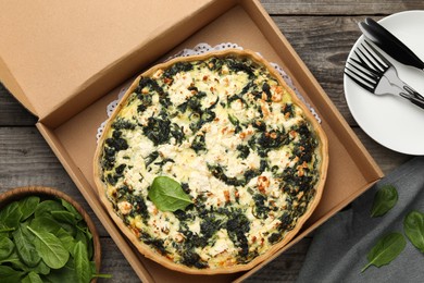 Photo of Delicious homemade spinach quiche in box and cutlery on wooden table, flat lay