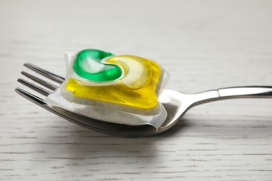 Fork with dishwasher detergent pod on white wooden table, closeup