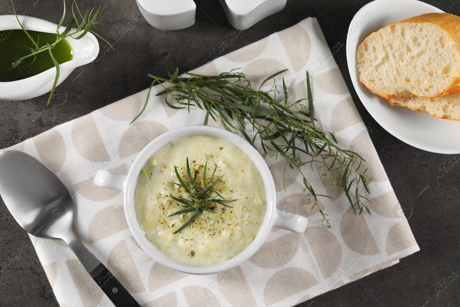 Photo of Delicious cream soup with tarragon, spices and potato in bowl served on dark textured table, flat lay