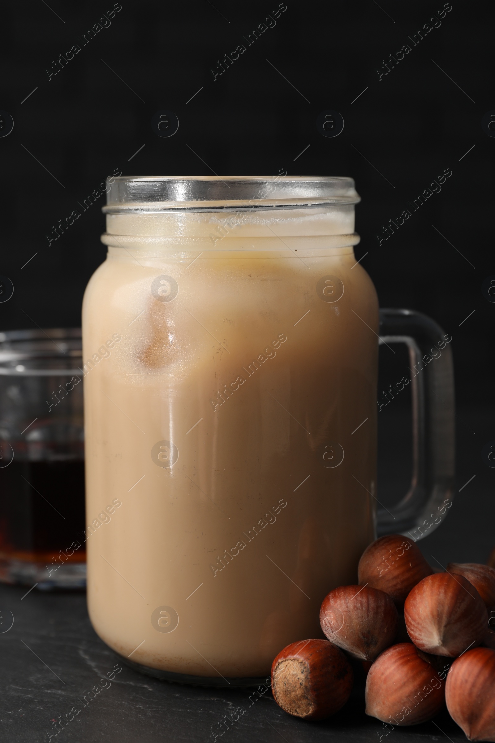 Photo of Mason jar of delicious iced coffee, syrup and hazelnuts on black table