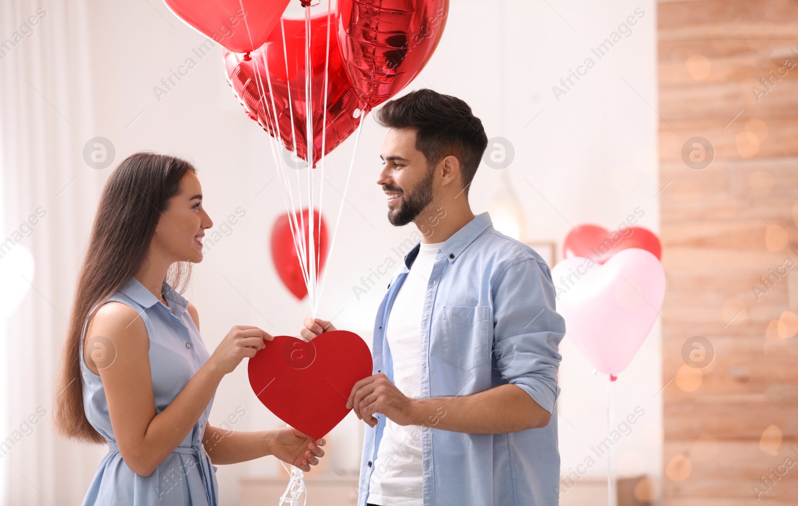 Photo of Lovely couple with heart shaped balloons in living room. Valentine's day celebration