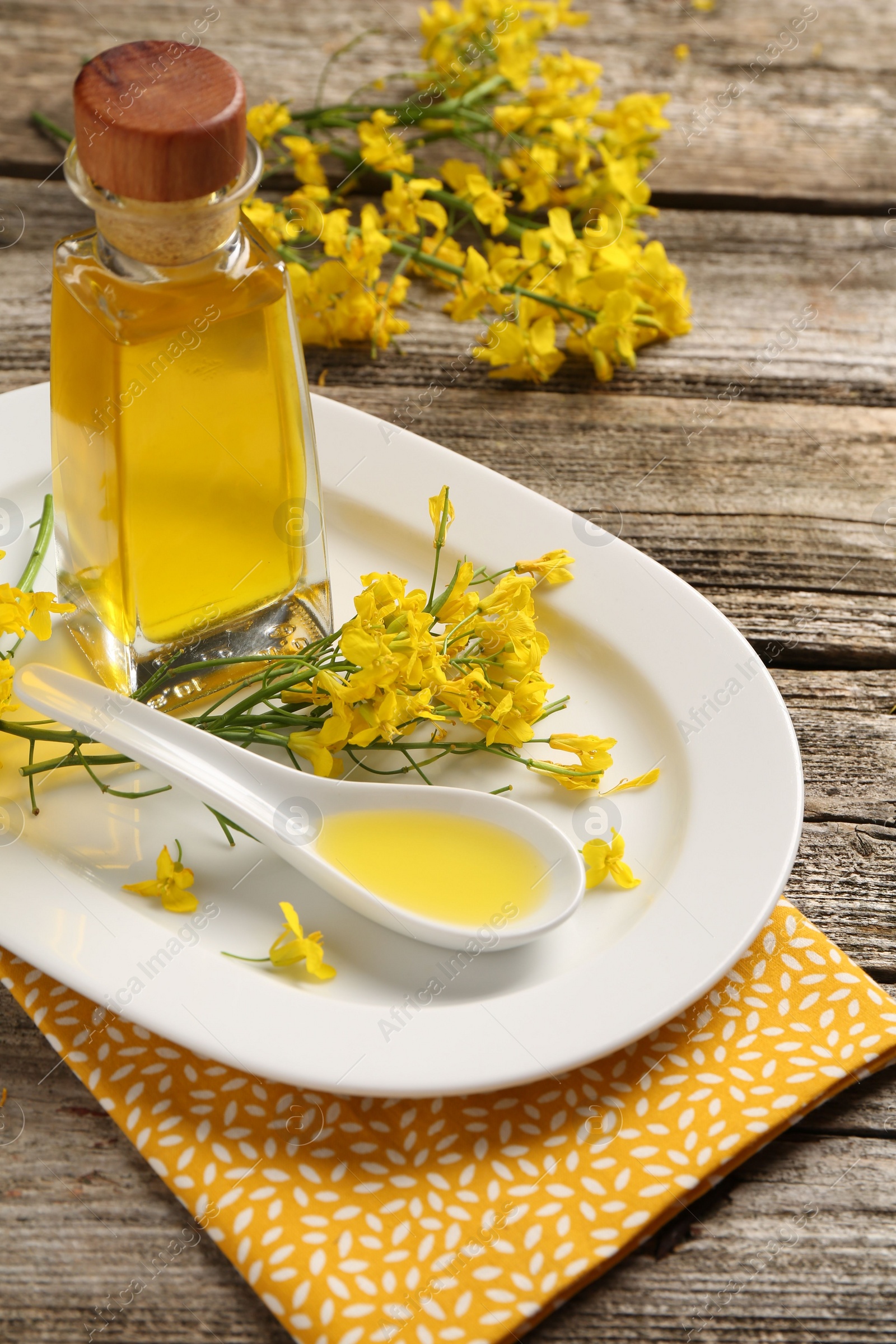 Photo of Rapeseed oil in glass bottle, gravy boat and beautiful yellow flowers on wooden table