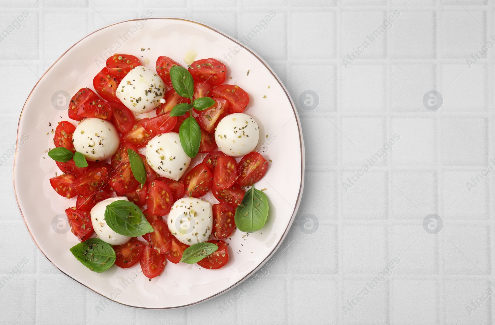 Photo of Tasty salad Caprese with tomatoes, mozzarella balls and basil on white tiled table, top view. Space for text