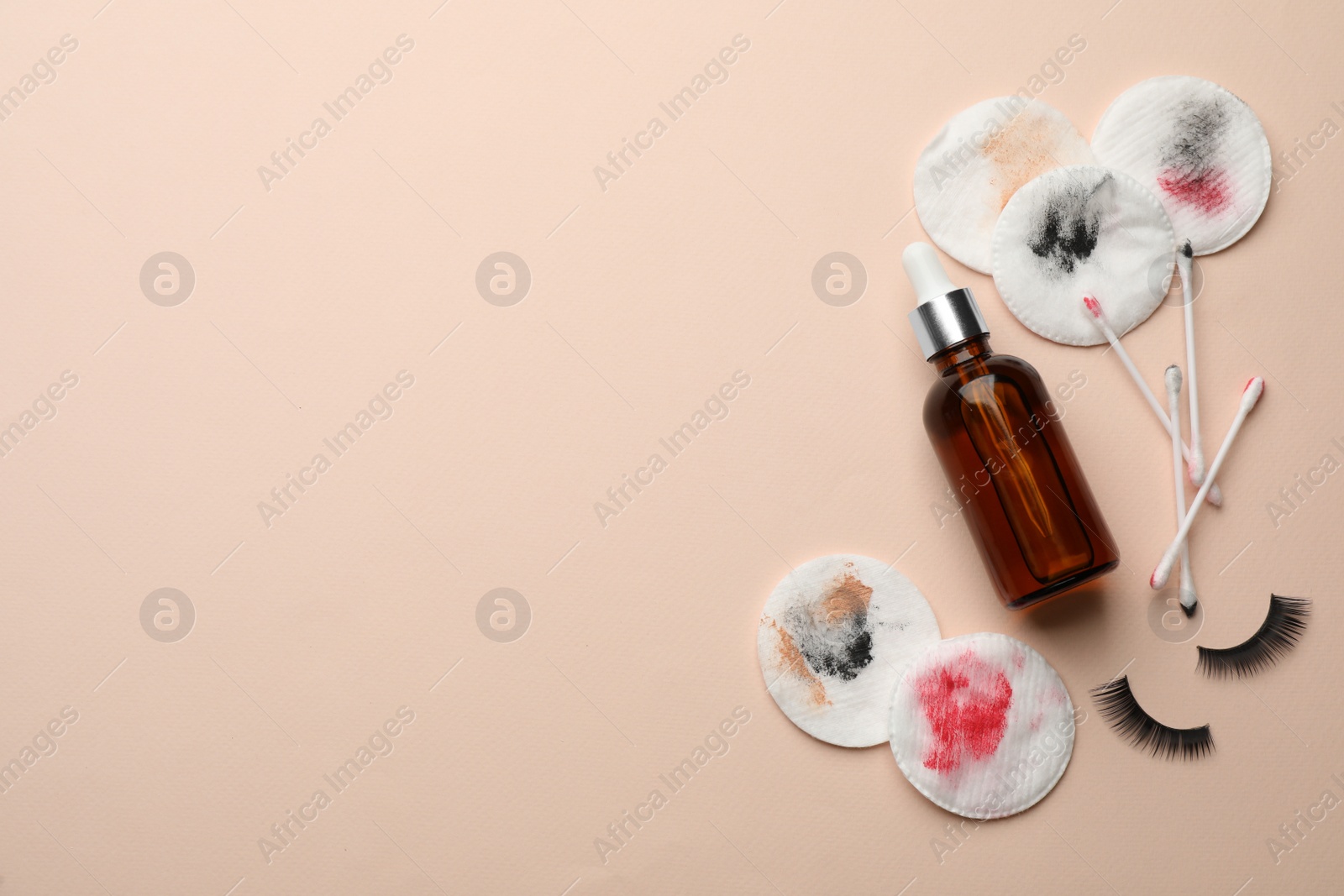 Photo of Dirty cotton pads, swabs, false eyelashes and makeup removal product on beige background, flat lay. Space for text