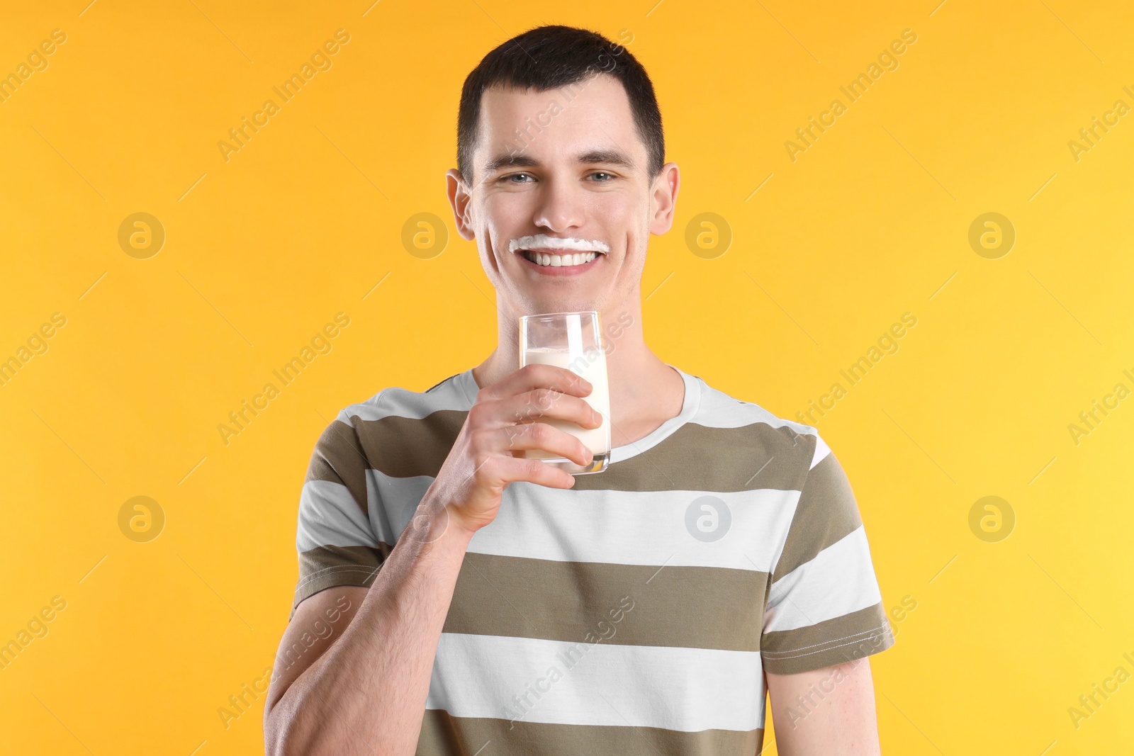 Photo of Happy man with milk mustache holding glass of tasty dairy drink on orange background