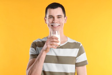 Photo of Happy man with milk mustache holding glass of tasty dairy drink on orange background