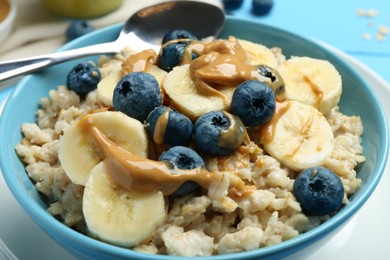 Tasty oatmeal with banana, blueberries and peanut butter served in bowl on table, closeup