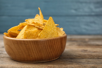 Bowl with tasty Mexican nachos chips on wooden table against blue background, space for text
