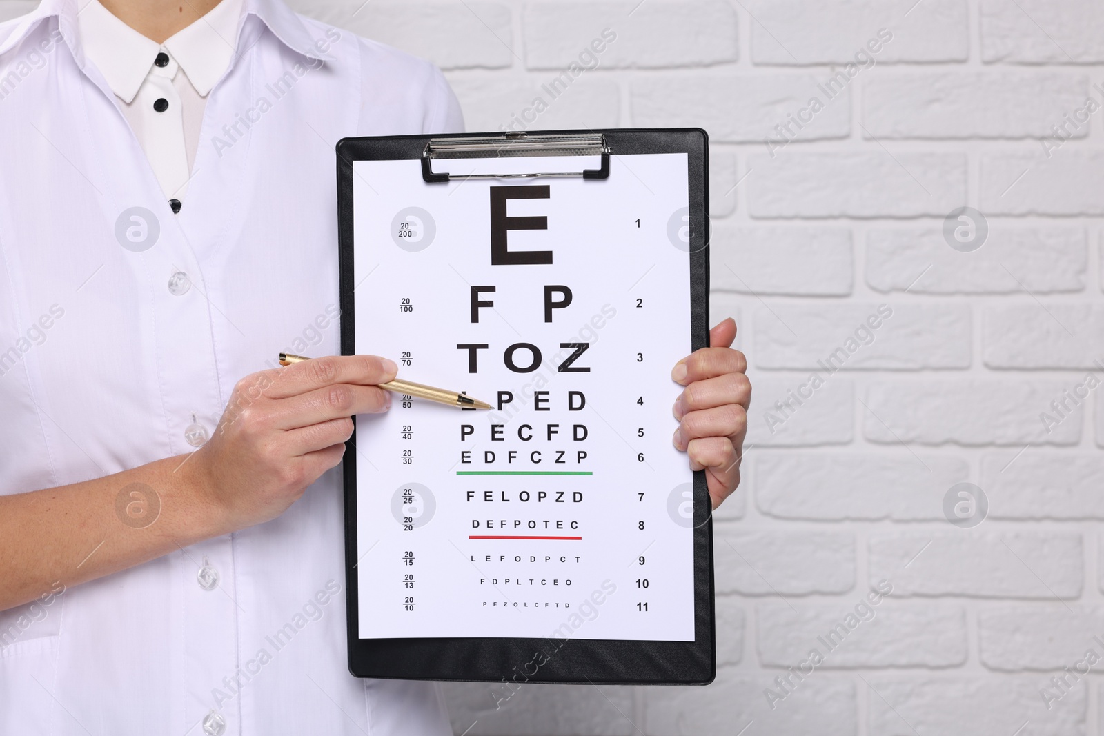 Photo of Ophthalmologist pointing at vision test chart near white brick wall, closeup. Space for text