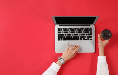 Photo of Woman with cup of coffee using modern laptop, top view. Space for text