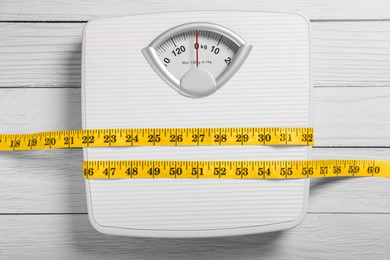 Scales with measuring tape on white wooden background, top view. Weight loss concept