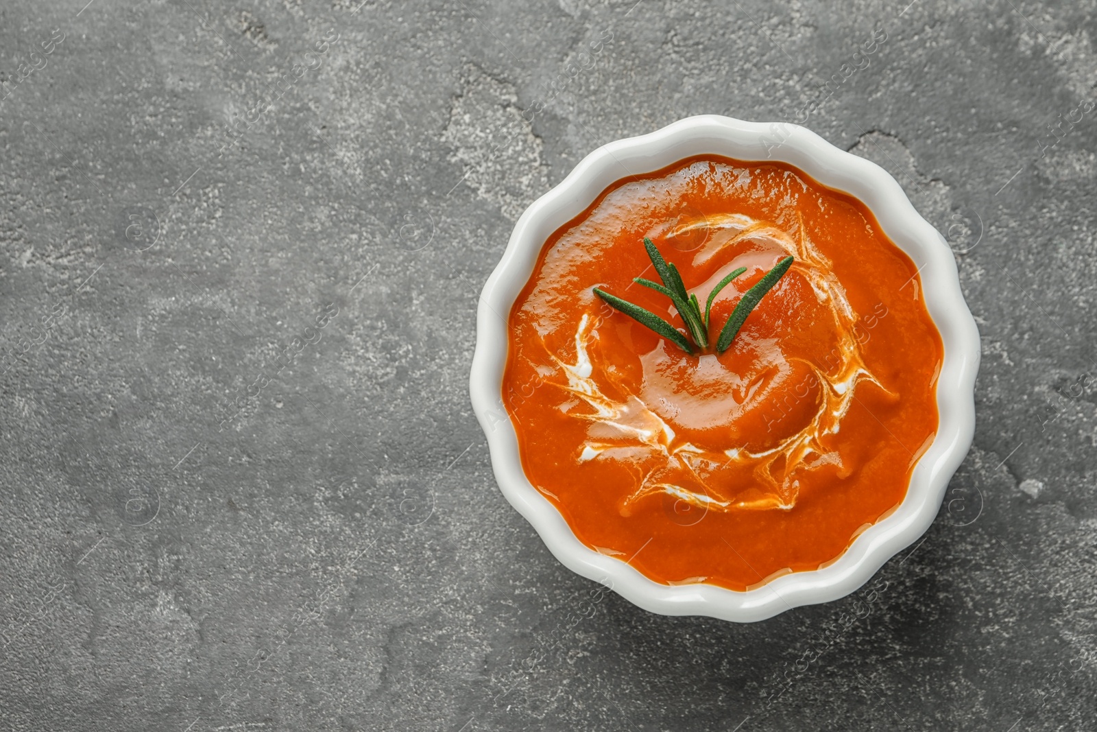 Photo of Bowl with fresh homemade tomato soup and space for text on grey background, top view