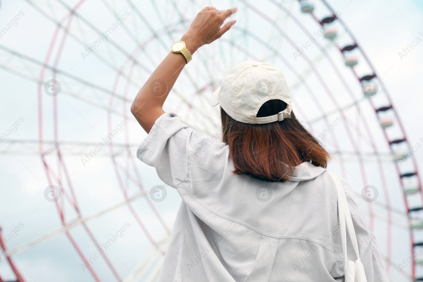 Photo of Young woman near Ferris wheel outdoors, back view