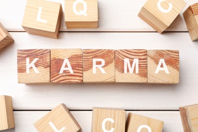 Word Karma made of cubes with letters on white wooden table, flat lay