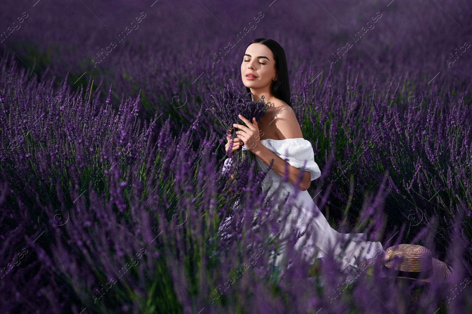 Photo of Beautiful young woman with bouquet sitting in lavender field