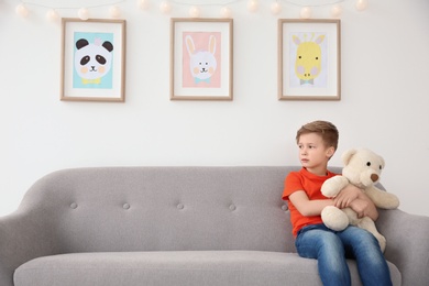 Little autistic boy sitting on sofa with toy at home