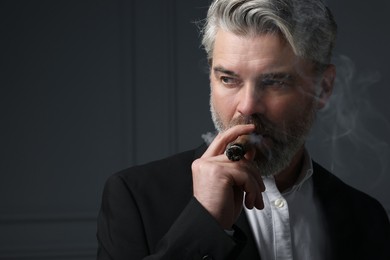 Photo of Handsome bearded man smoking cigar against dark grey background. Space for text