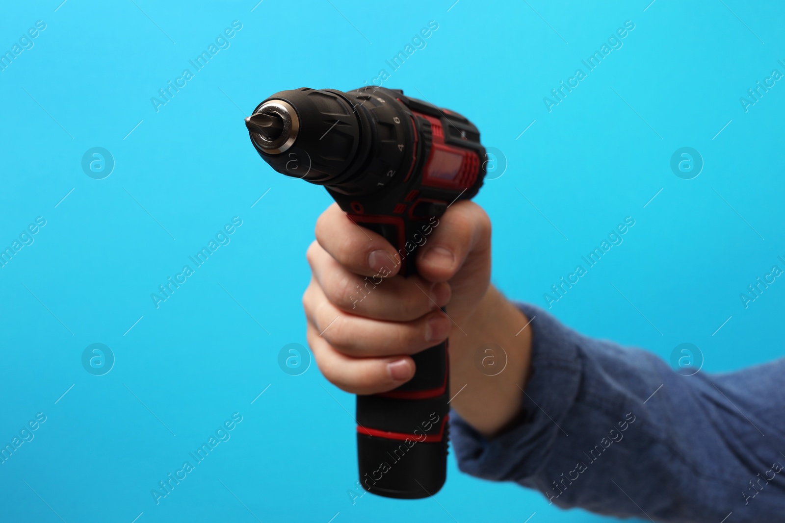 Photo of Handyman holding electric screwdriver on light blue background, closeup