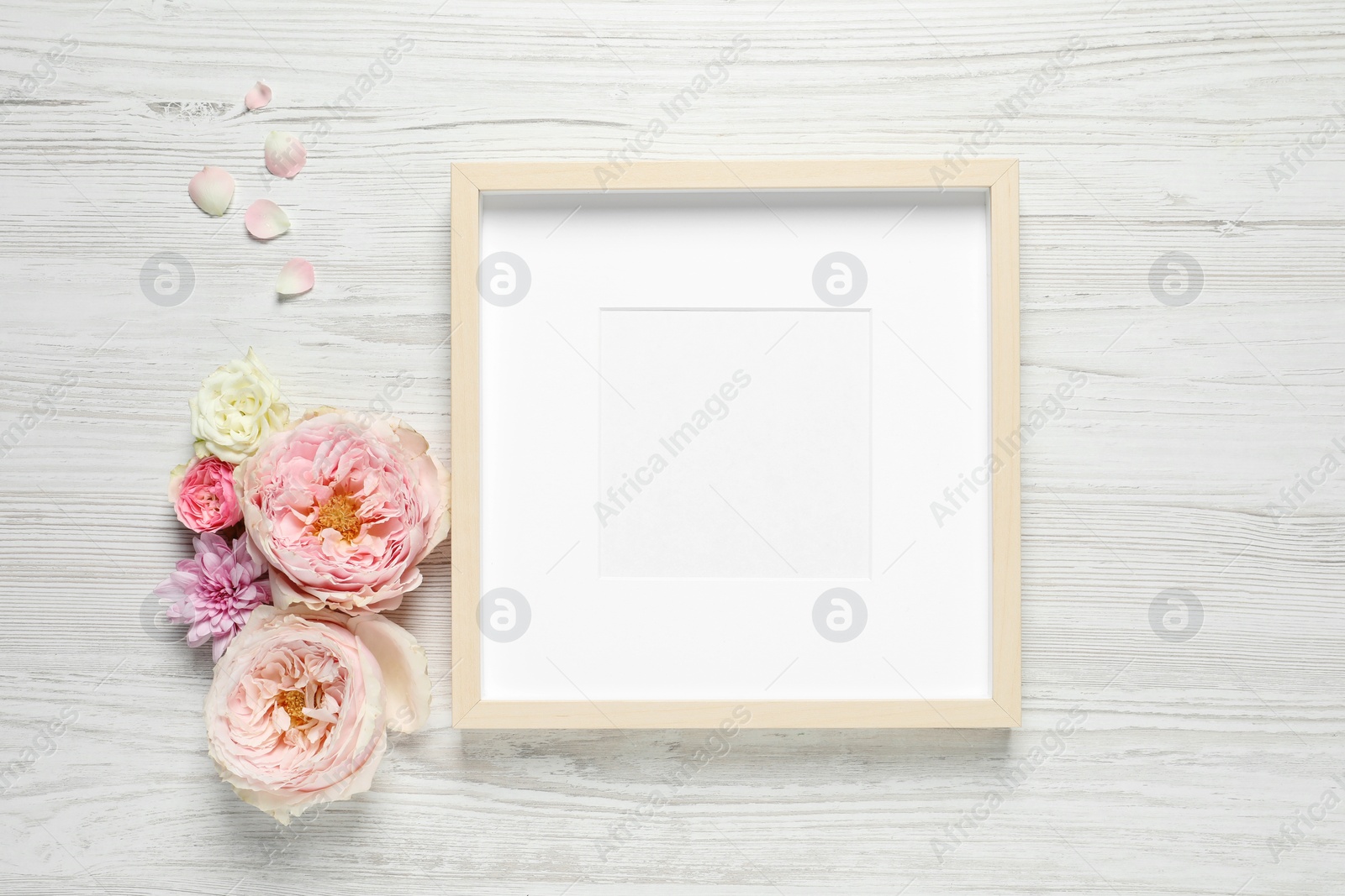 Photo of Empty photo frame and beautiful flowers on white wooden table, flat lay. Space for design