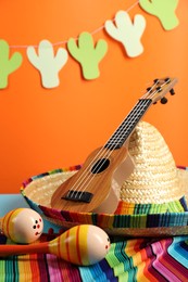 Mexican sombrero hat, maracas and ukulele on table, closeup