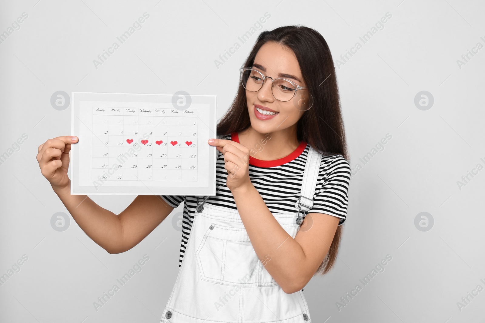 Photo of Young woman holding calendar with marked menstrual cycle days on light background