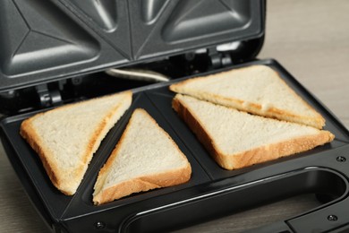 Modern sandwich maker with bread slices on wooden table, closeup