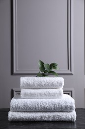 Photo of Stacked terry towels and green leaves on black textured table indoors, space for text