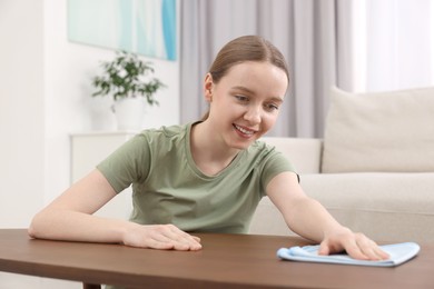 Photo of Woman with microfiber cloth cleaning wooden table in room