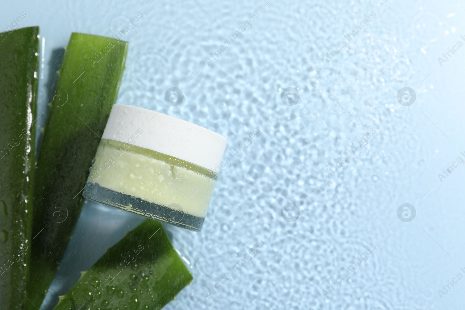 Photo of Jar of cosmetic product and aloe leaves in water on light blue background, flat lay. Space for text