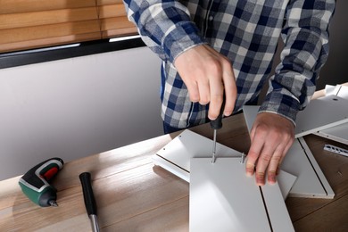 Man assembling furniture at table indoors, closeup