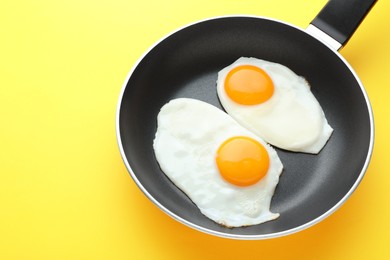 Photo of Tasty fried eggs in pan on yellow background, above view