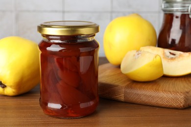 Photo of Tasty homemade quince jam in jar and fruits on wooden table, closeup