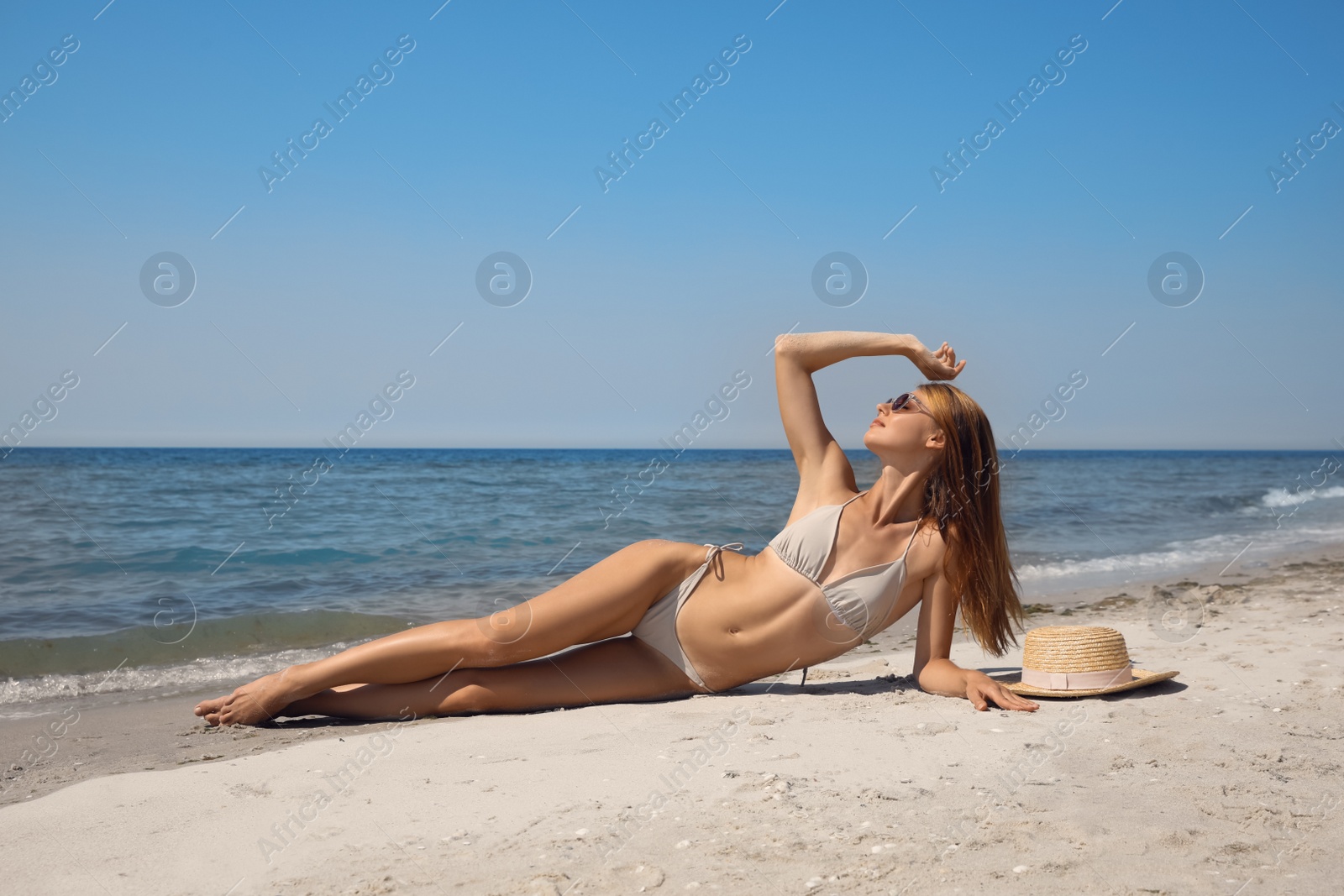 Photo of Attractive woman with perfect body in bikini lying on sandy beach near sea
