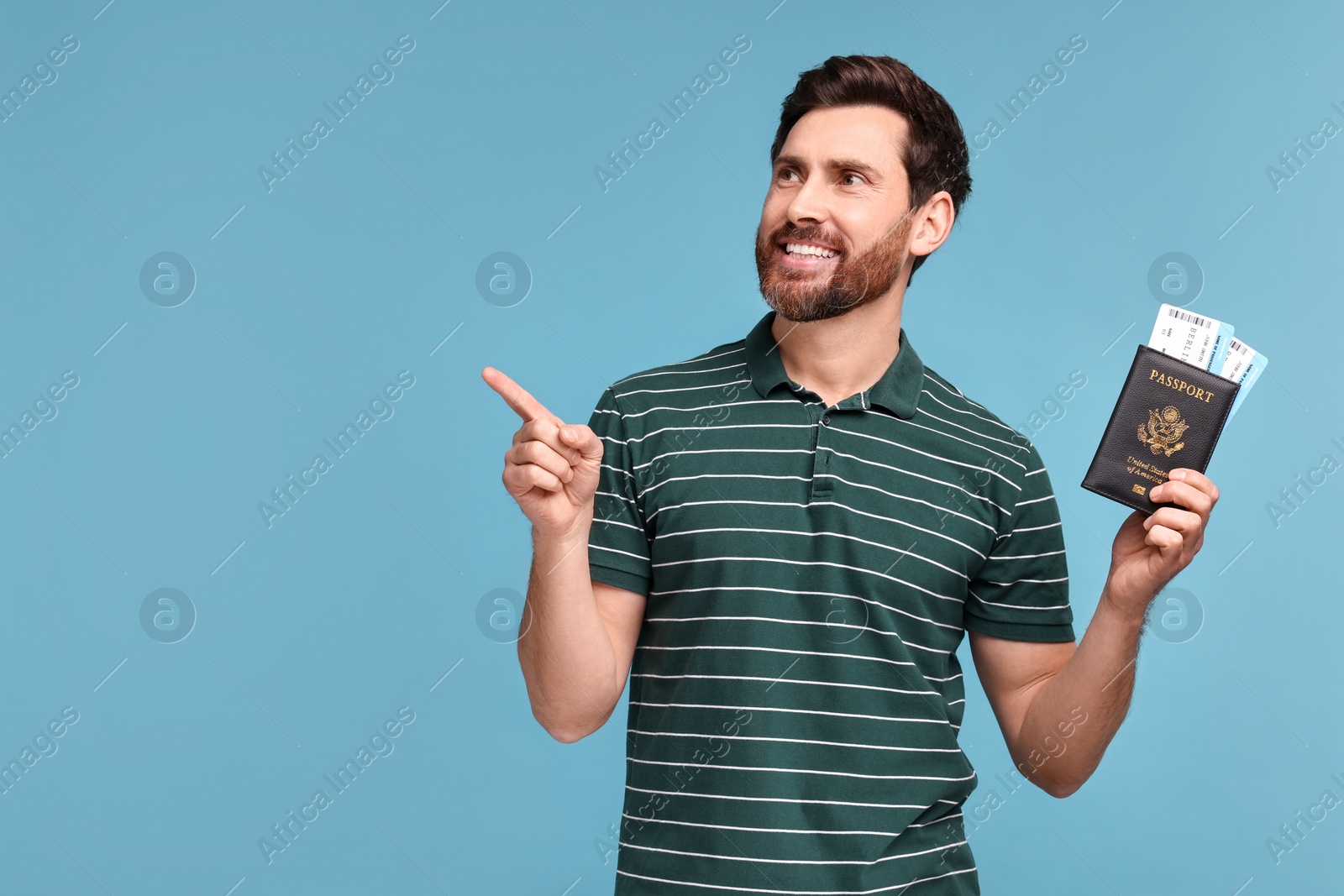 Photo of Smiling man with passport and tickets pointing at something on light blue background. Space for text