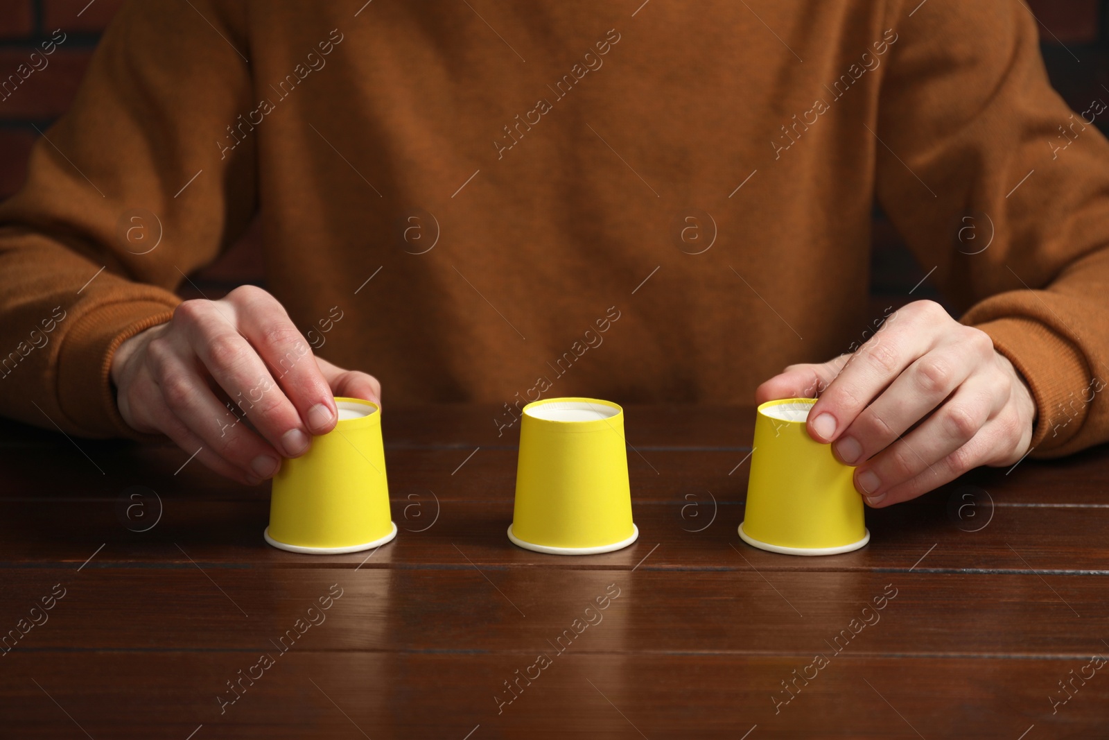 Photo of Man playing shell game at wooden table, closeup