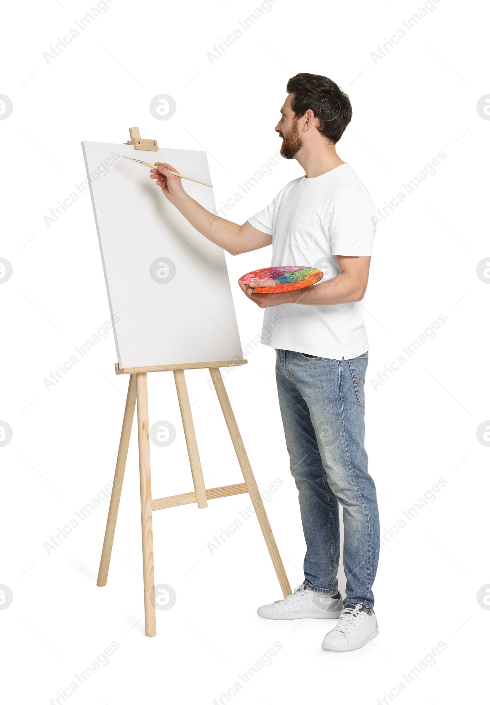 Photo of Man with brush painting against white background. Using easel to hold canvas