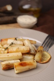 Photo of Baked salsify roots, lemon, thyme and fork on plate, closeup