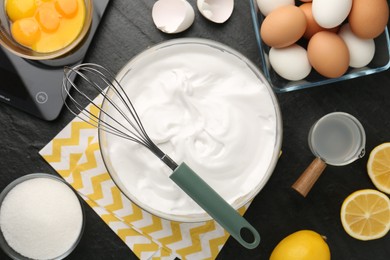 Bowl with whipped cream, whisk and ingredients on black table, flat lay