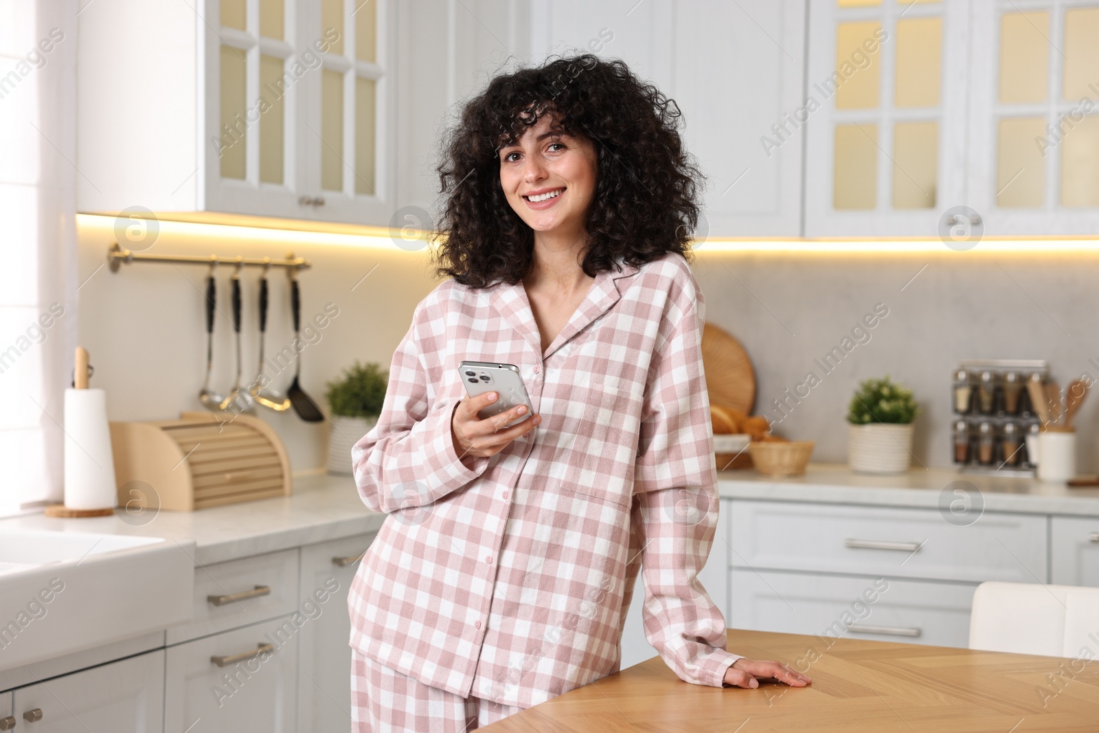 Photo of Beautiful young woman in stylish pyjama with smartphone in kitchen